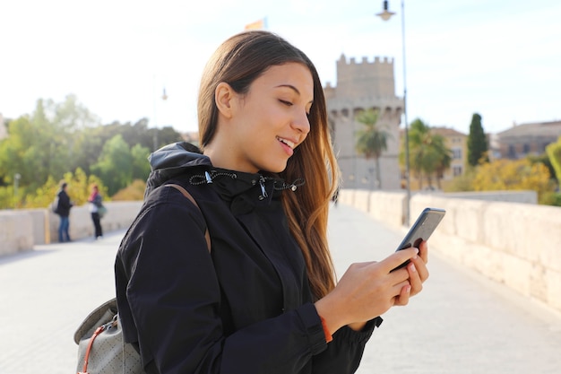 Happy young woman walking in the city sending text message on phone in autumn or winter