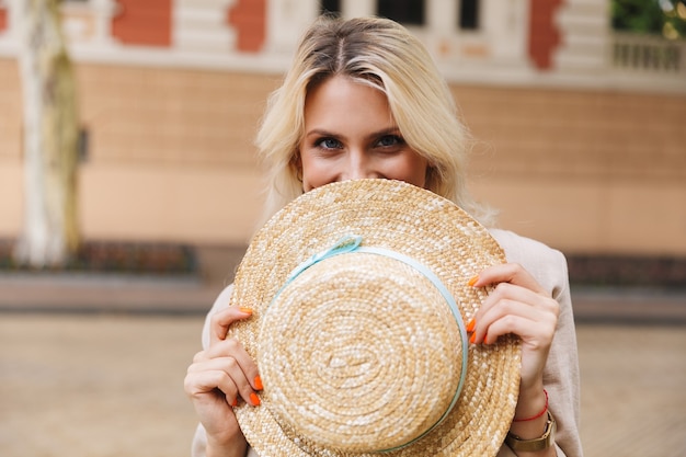 happy young woman walking outdoors holding hat in hands covering eyes