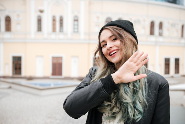 Happy young woman walking on street while waving.