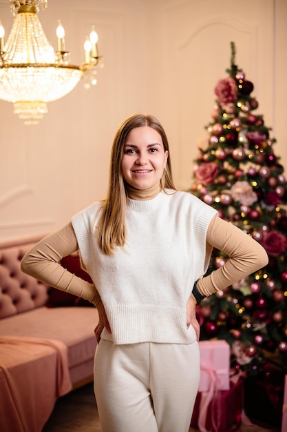 Happy young woman in a white knitted suit on the background of festive Christmas trees New Year's atmosphere