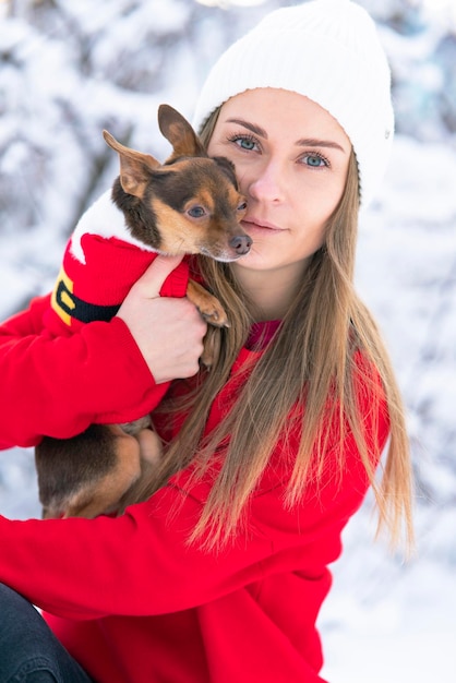 Happy young woman in winter holds in her arms and plays in the snow with her dog chihuahua kissing p...