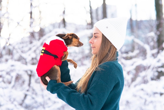 Happy young woman in winter holds in her arms and plays in the snow with her pet chihuahua dog