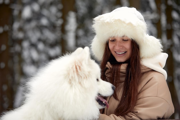 Happy young woman in winter holds in her arms and plays in the snow with her pet dog