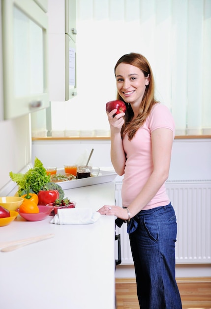 happy young  woman with apple in kitchen and other food and vegetables