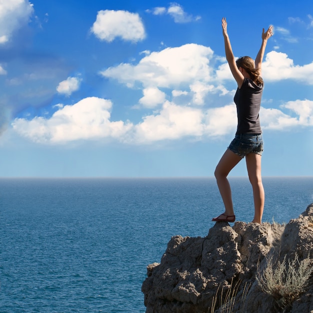 Happy young woman with arms raised against blue sky with clouds.