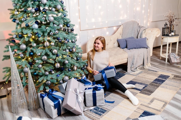 Happy young woman with a gift lying near the Christmas tree White silver color on sofa background Merry Christmas and New Year Atmospheric moments