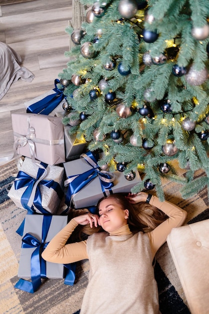 Happy young woman with a gift lying near the Christmas tree White silver color on sofa background Merry Christmas and New Year Atmospheric moments