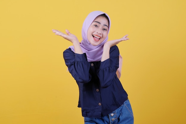 Happy young woman with happy facial expression shows something in her hand wearing hijab and casual clothes in yellow