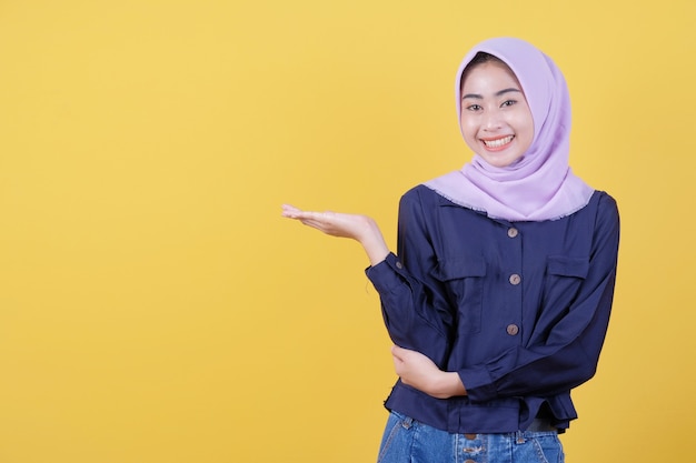 Happy young woman with happy facial expression shows something in her hand wearing hijab and casual clothes in yellow