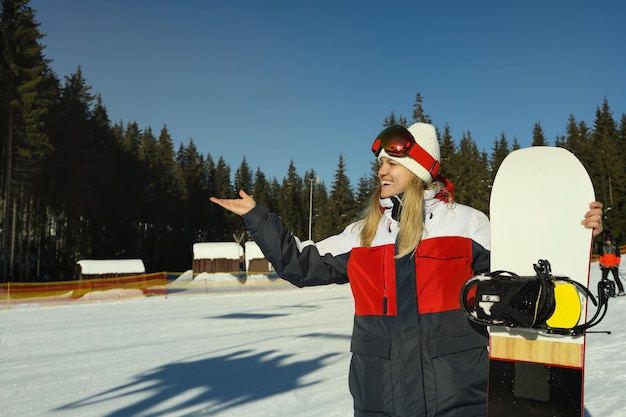 Happy young woman with snowboard in mountain resort