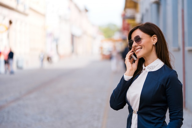 Happy young woman with sunglasses speaks by phone on the street