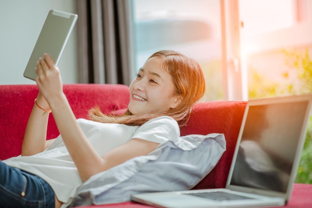 Happy young woman with tablet laying on sofa and  have a laptop.