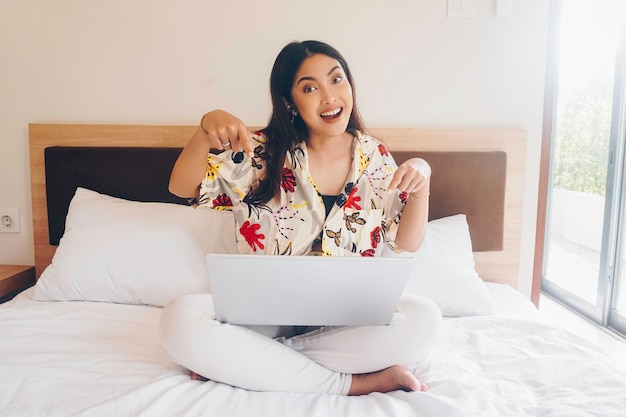 Happy young woman working from the bed Hold the laptop on the knees and type on the keyboard