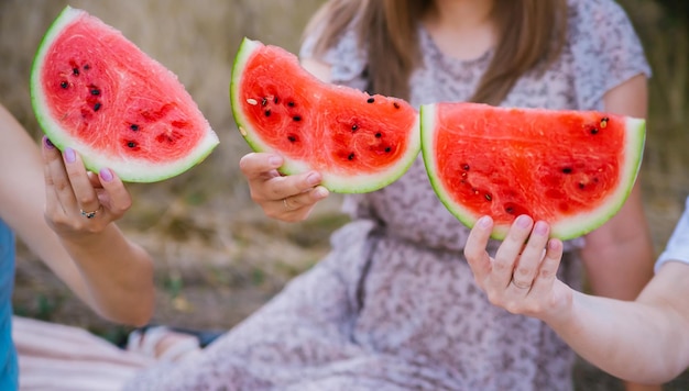 Happy young women hold slices of watermelon outdoors Closeup of watermelon slices Bright red berry Juicy sweet snack in summer on a picnic