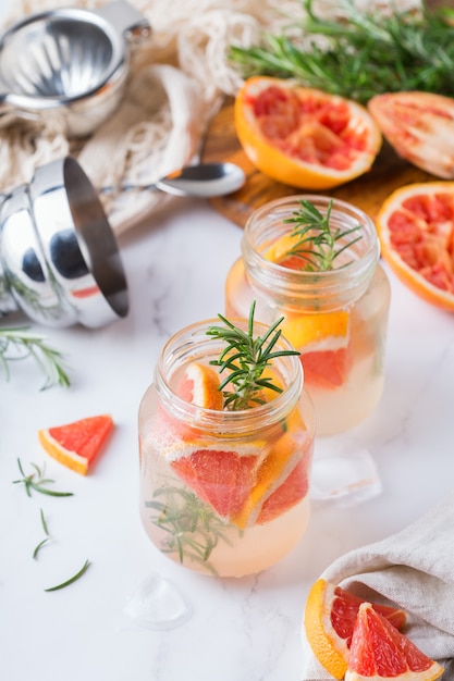 Hard seltzer cocktail with grapefruit, rosemary and ice on a table. Summer refreshing beverage, drink on a white table