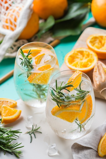 Hard seltzer cocktail with orange, rosemary and ice on a table. Summer refreshing beverage, drink with trendy zero waste accessories, bamboo straw and mesh bag.