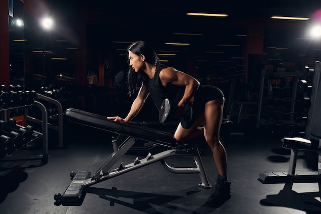 Hard-working fit woman lifting weights on an incline bench while exercising at the gym