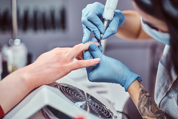 Hardware manicure in a beauty salon. Manicure procedure in progress - Beautician master using nail drill to trim and remove cuticles