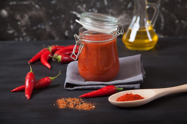 Harissa spicy herb in a glass jar stands on a gray linen napkin, a wooden spoon with spices, oil and chili pepper. Traditional national cuisine.