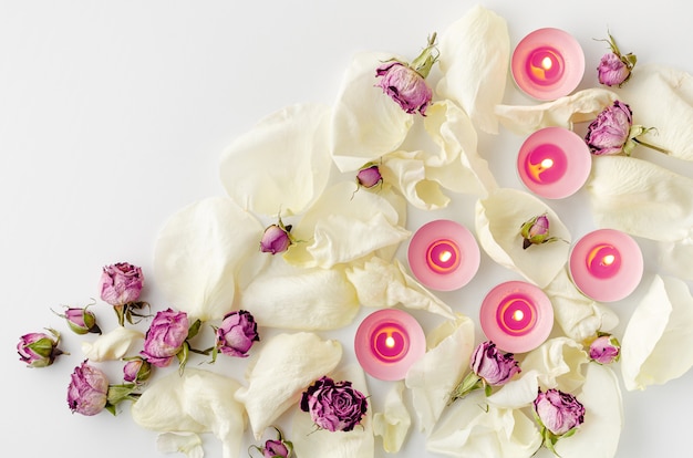 Harmony concept. Burning aroma candles, dried roses and petals on white. Flat lay, copy space