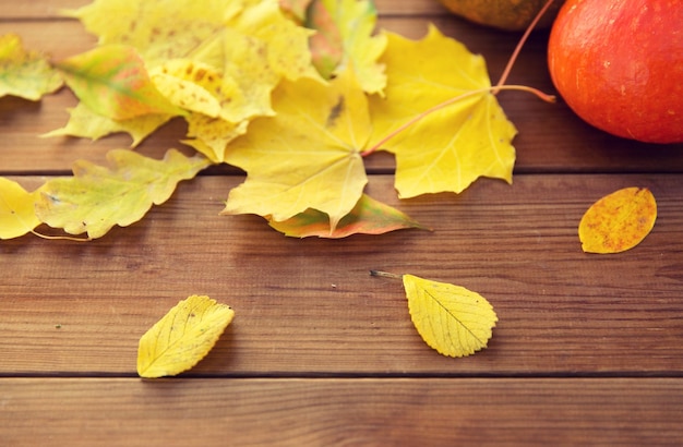 harvest, season, advertisement and autumn concept - close up of pumpkins and leaves on wooden table at home