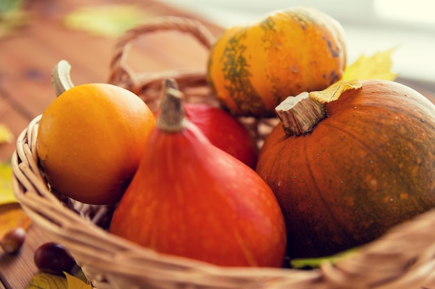 harvest, season, advertisement and autumn concept - close up of pumpkins in wicker basket with leaves on wooden table at home