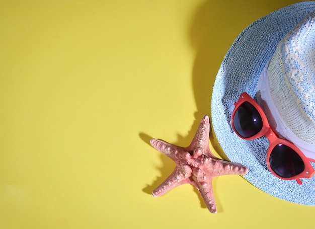 A hat and sunglasses are on a yellow background with a starfish and a starfish.