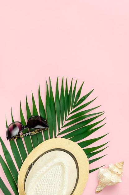 Hat, sunglasses and palm leaf on pastel pink background. Top view, copy space.