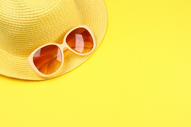 Hat, sunglasses on a pastel yellow background.