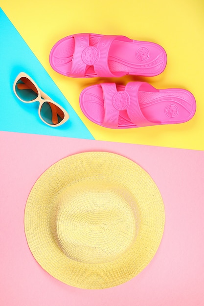 Hat, sunglasses and slippers on three-color pastel background of blue, yellow and pink.