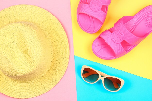 Hat, sunglasses and slippers on a three-color pastel background of blue, yellow and pink.