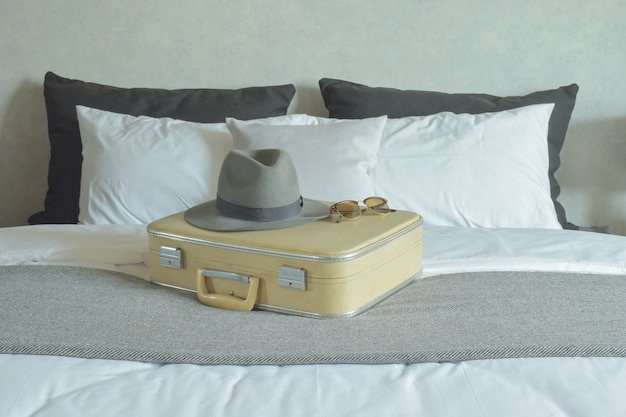 Hat, sunglasses and vintage travel bag setting on bed