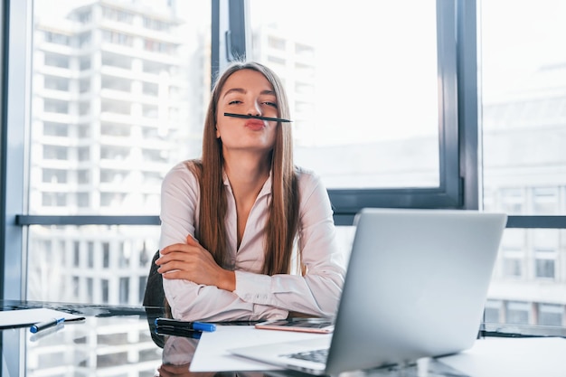 Have fun at break Young woman in white formal clothes is indoors in the modern office