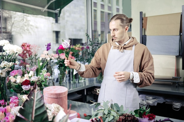 Have a look. Handsome stylish florist wearing apron while working in floral shop