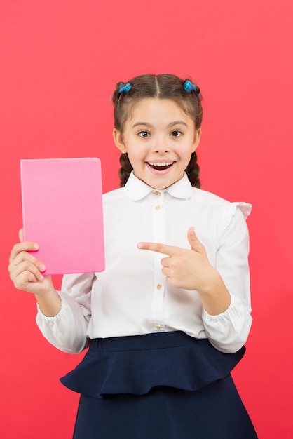 Having access to information through books. Small child got information on red background. Little girl pointing finger at book for information. Spread information and gather knowledge, copy space.