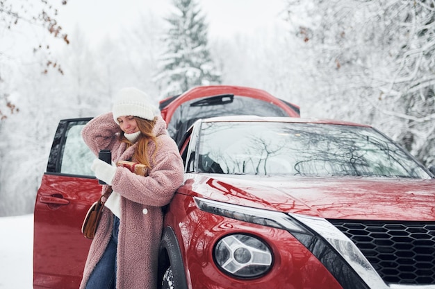 Having fun Beautiful young woman is outdoors near her red automobile at winter time