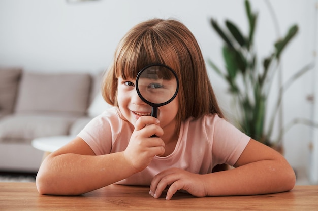 Having fun Little girl is sitting by the table with magnifying glass