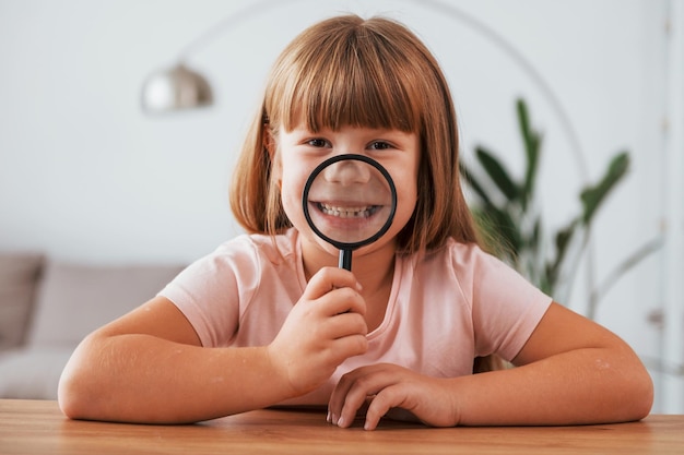 Having fun Little girl is sitting by the table with magnifying glass