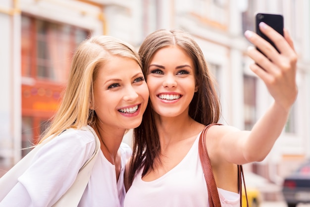 Having fun together. Two beautiful young women making selfie and smiling while standing outdoors