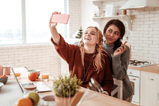 Having meeting. Beautiful long-haired girls making selfie together in kitchen while eating healthy snacks