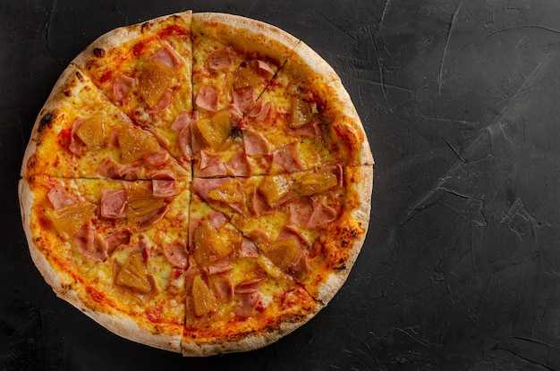 Hawaiian pizza prepared in a wood-fired oven. Black background. Flat view