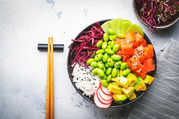 Hawaiian poke bowl with salmon avocado radish edamame beans red cabbage and white rice Soy sauce lime and sesame dressing White table background top view