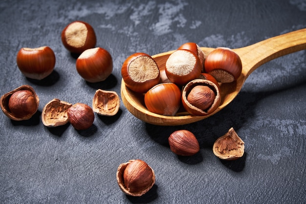 Hazelnut in wooden spoon on black table, close-up.