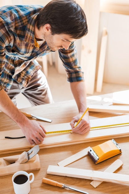 He has an eye for detail. Confident young male carpenter making measurements on the wooden plank