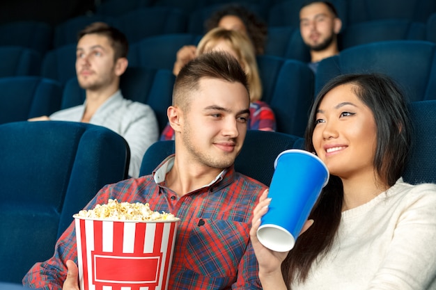 He loves to see her smiling. Young handsome man looking warmly at his girlfriend while she is enjoying her drink watching a movie in the cinema