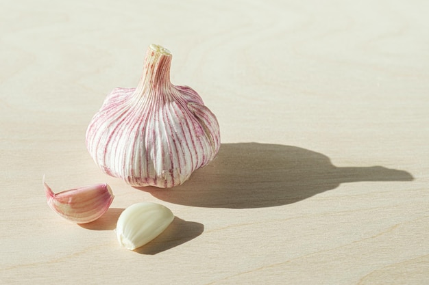 Head of fresh garlic and two cloves of garlic on light wooden background