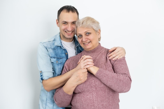 Head shot happy young bearded man embracing beautiful smiling middle aged senior mother in eyewear, relaxing together on comfortable sofa in living room, enjoying funny conversation or gossiping.