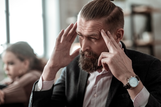 Headache after conflict. Bearded dark-haired father having headache after conflict with teenage daughter