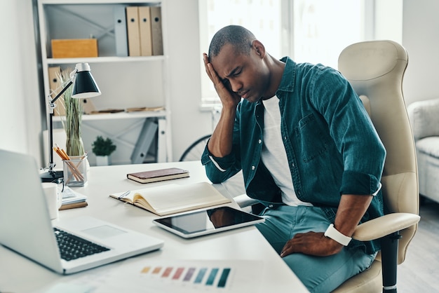 Headache. Frustrated young African man in shirt making a face while sitting in the office