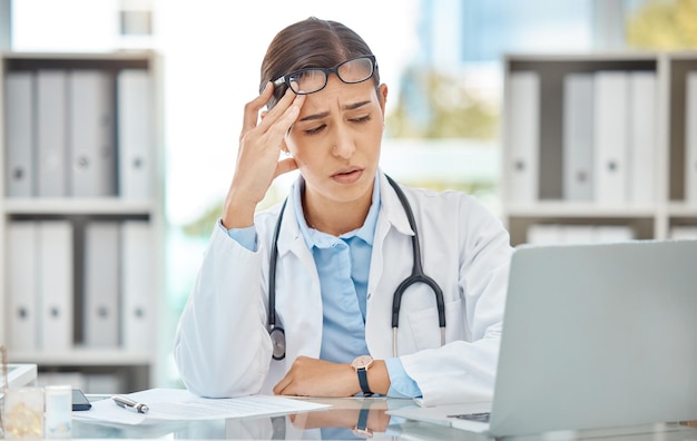 Headache stress doctor burnout and sad nurse working on laptop in work office at hospital tired from consulting in healthcare and anxiety from medical surgery Worker with depression at clinic